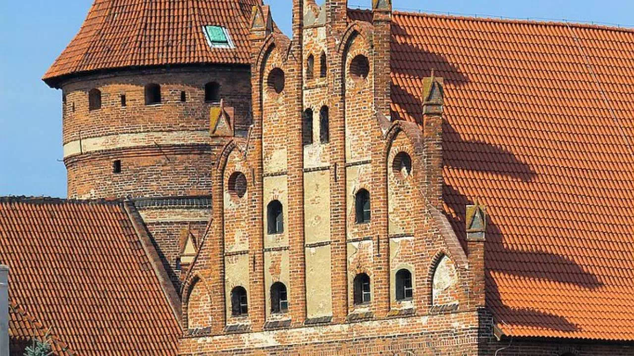 Zamek, który znajduje się w pobliżu Starego Miasta w Olsztynie. Widok na jego zabudowę z czerwonej cegły i wieżę w kształcie rotundy.