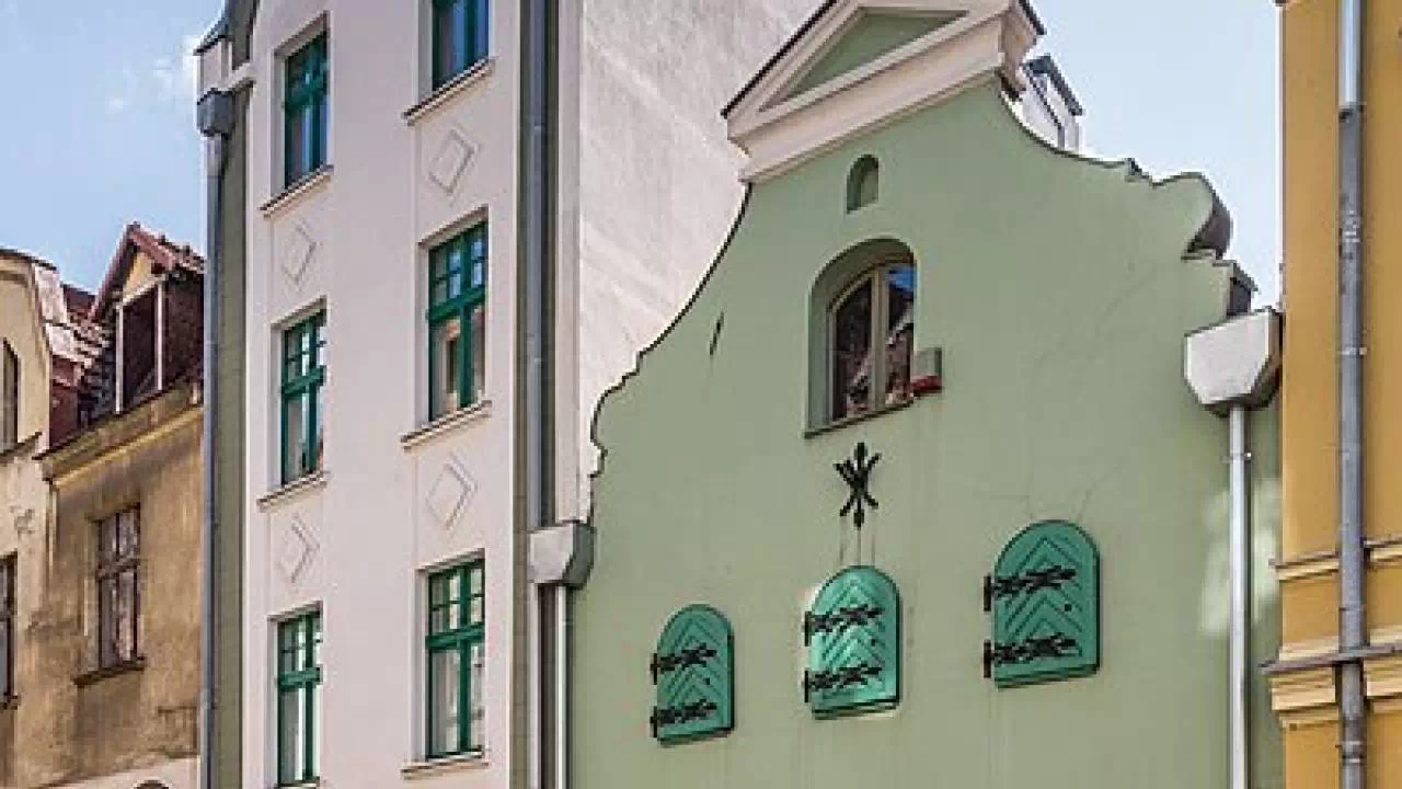 Zielony smukły budynek, czyli Muzeum Podróżników w Toruniu, który mieści się w zabytkowej kamienicy.