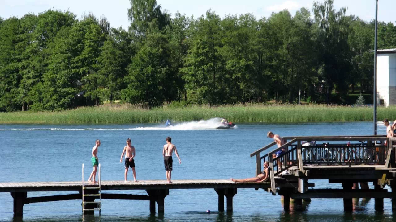 Plaża miejska przy jeziorze Ukiel i pomost, na którym stoją młodzi chłopcy.