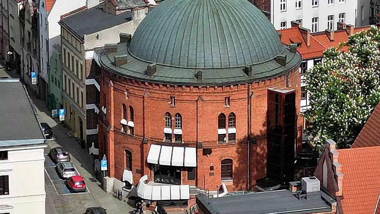 Budynek Planetarium w Toruniu. Obiekt z czerwonej cegły w kształcie rotundy otoczony wieloma budynkami starego miasta.