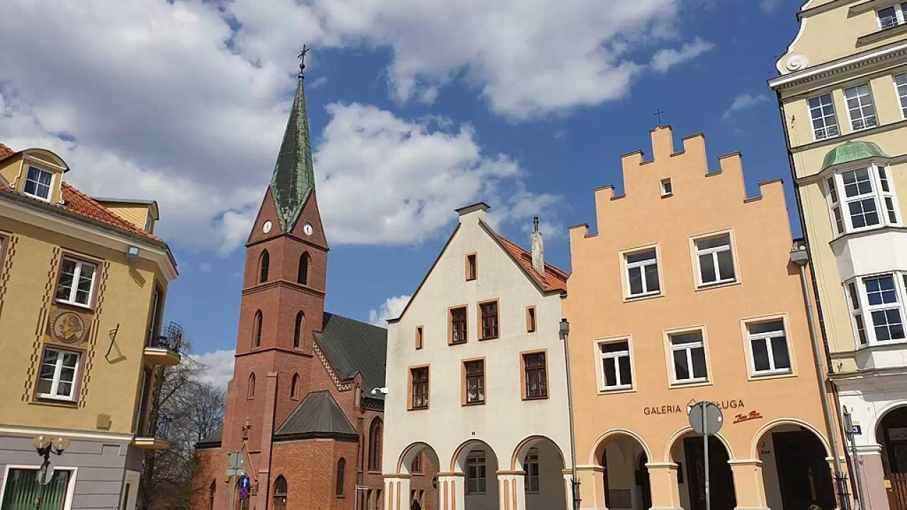 Zdjęcie Starego Miasta w Olsztynie z zabudową kamieniczek oraz kościołem oraz placem.